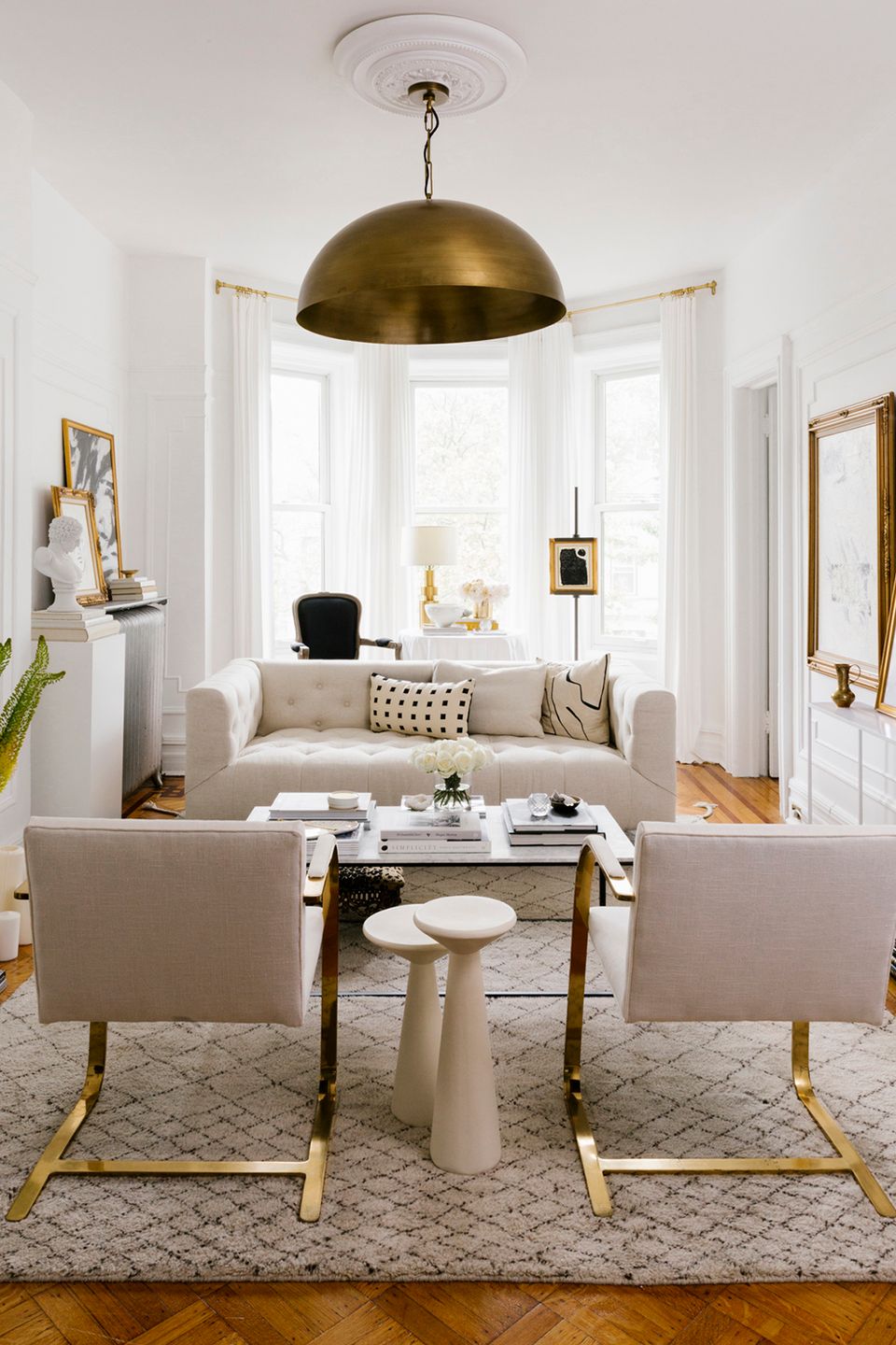 Contemporary living room in soft neutrals with brass dome pendant, cream furnishings, and geometric rug creating elegant simplicity.