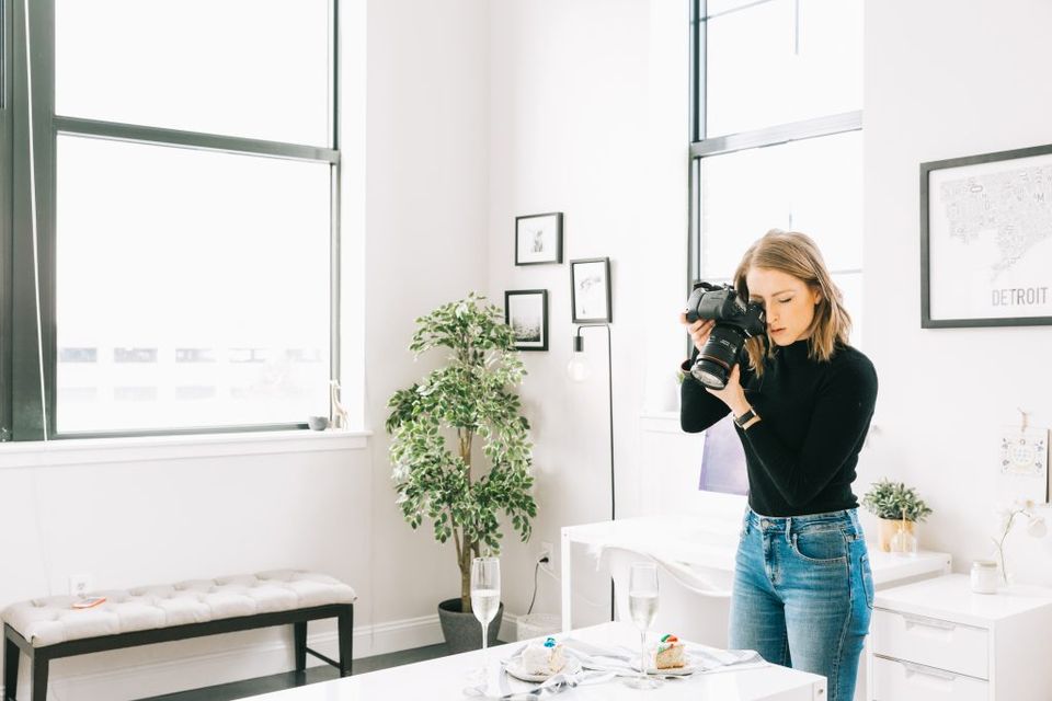 Minimalist workspace featuring tall windows, cascading plant, and clean white shelving against soft gray walls