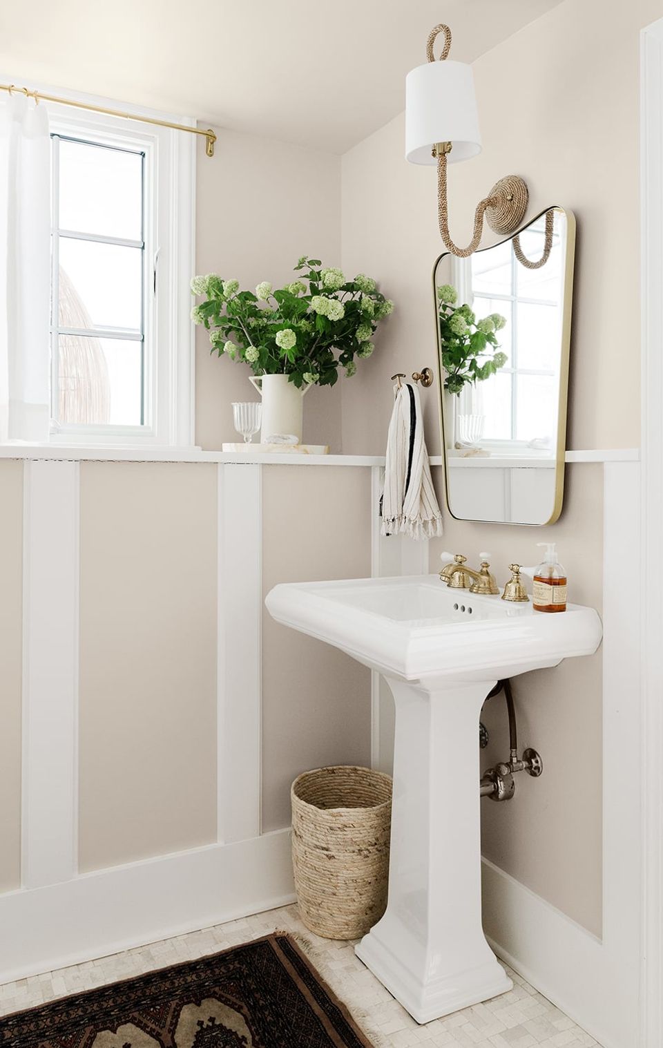 Classic greige bathroom with wainscoting, pedestal sink, and fresh floral arrangement