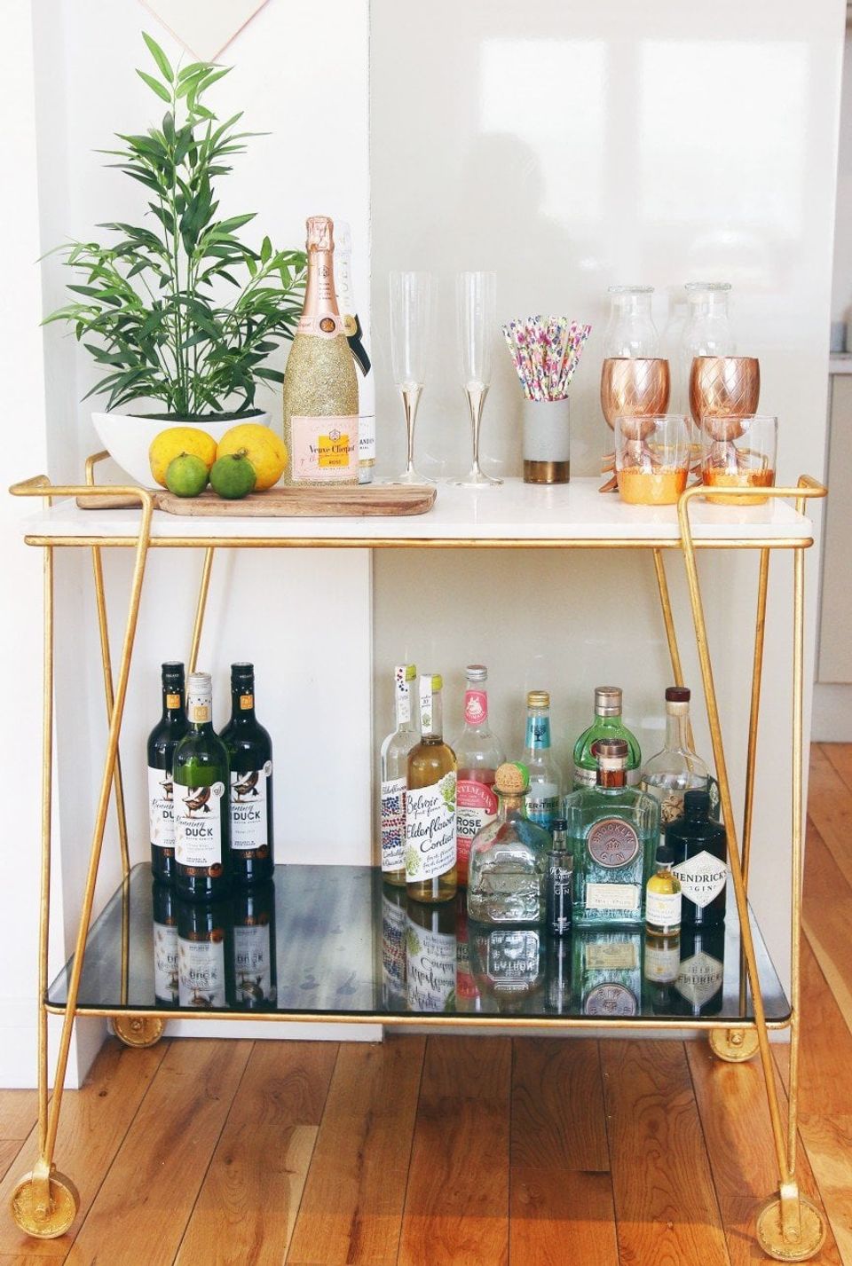 Mid-century modern bar cart with brass frame, greenery, champagne, and glassware in warm, minimalist style