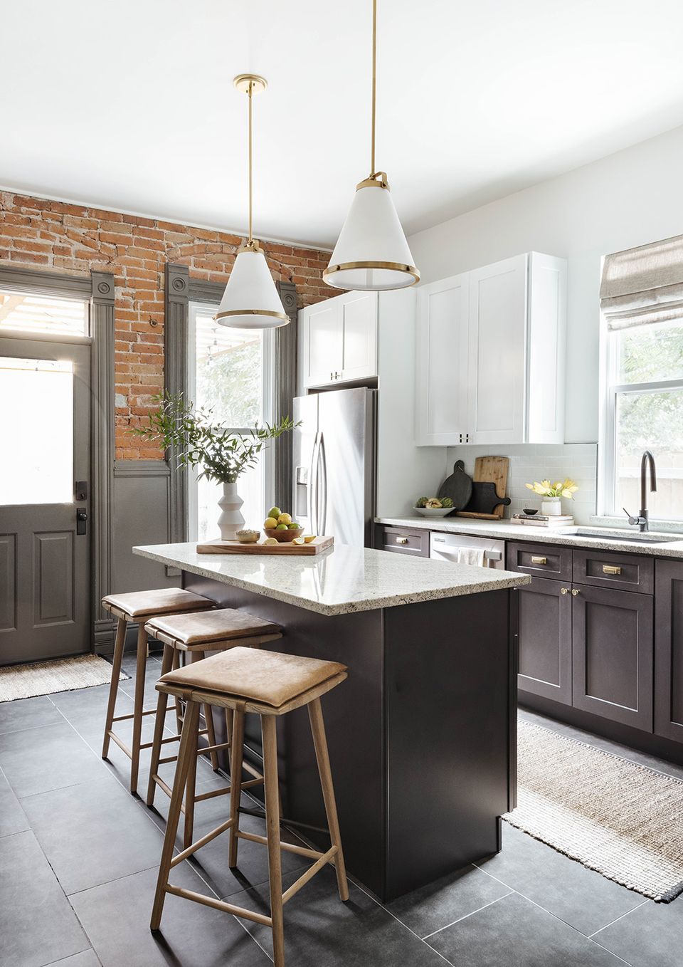Modern farmhouse kitchen combining exposed brick, white cabinetry, black island, and warm wood barstools