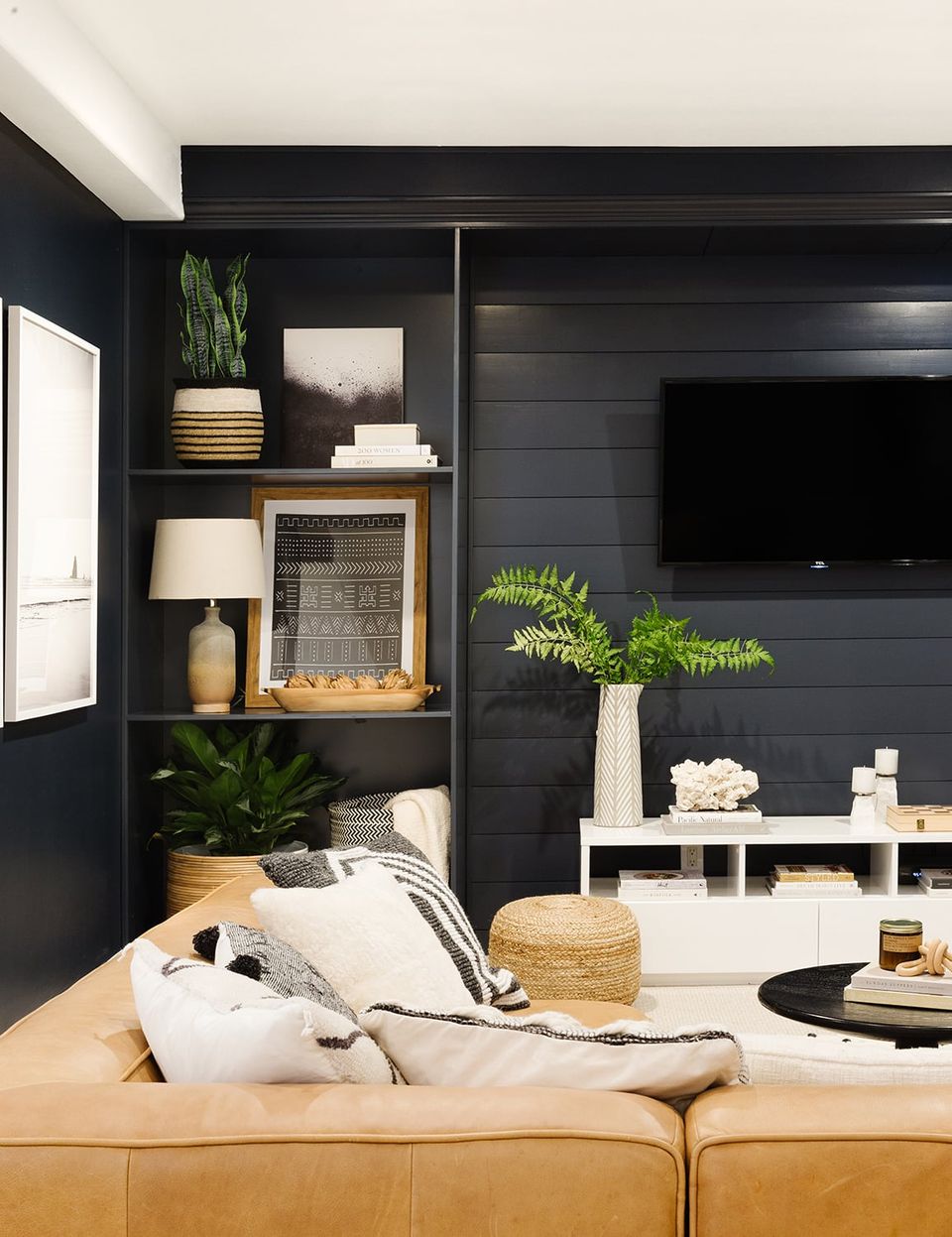 Cozy dark basement with black shiplap walls, warm leather seating, and botanical greenery accents