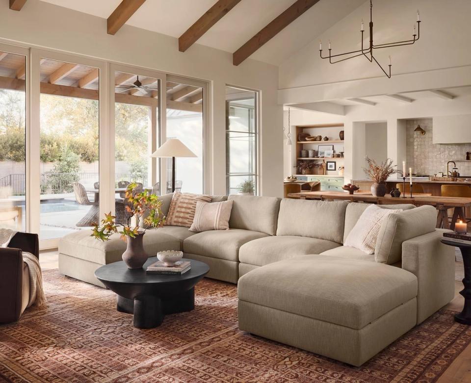Warm contemporary living room with neutral gray sectional, exposed wood beams, muted terracotta rug, and abundant natural light