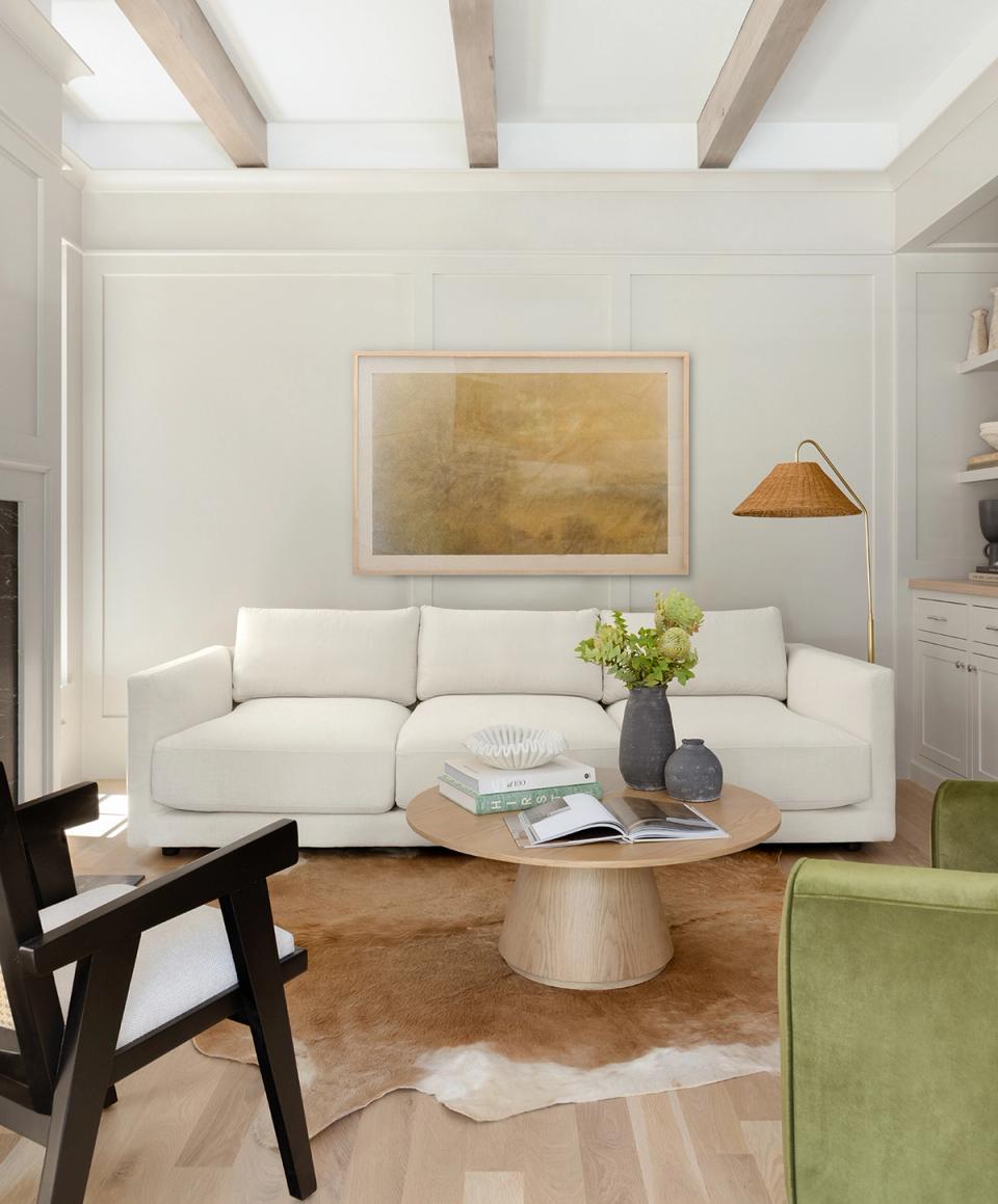 Neutral contemporary space with cream sofa, round wood table, and scattered hide rug