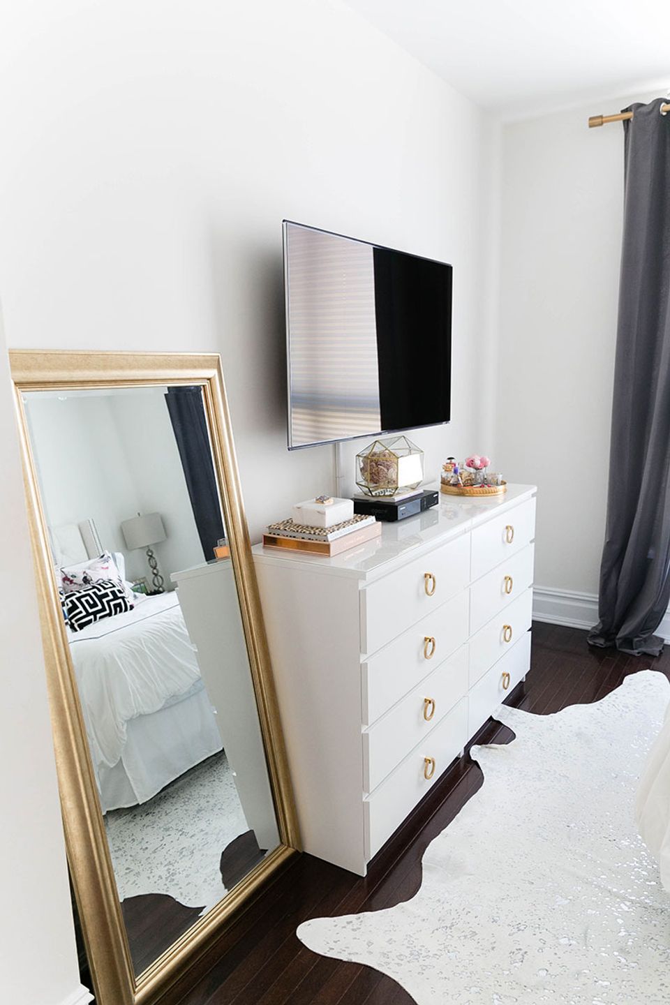Modern minimalist dorm with white dresser, gold-framed mirror, and clean monochromatic scheme