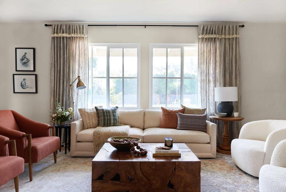 Warm greige living room with burgundy chairs, beige sofa, and wood coffee table by large windows