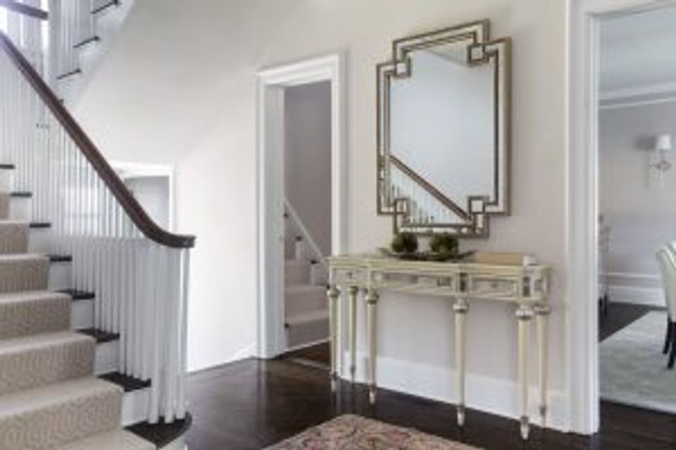 Classic foyer with pale blue console table, geometric mirror, dark staircase, and timeless elegance