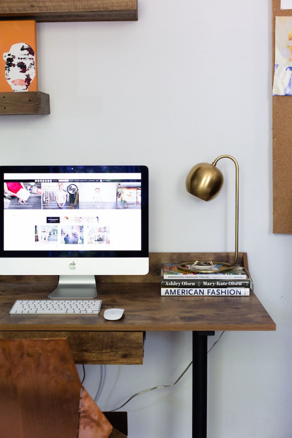 Industrial workspace featuring brass arc lamp, reclaimed wood desk, and minimalist white wall styling.