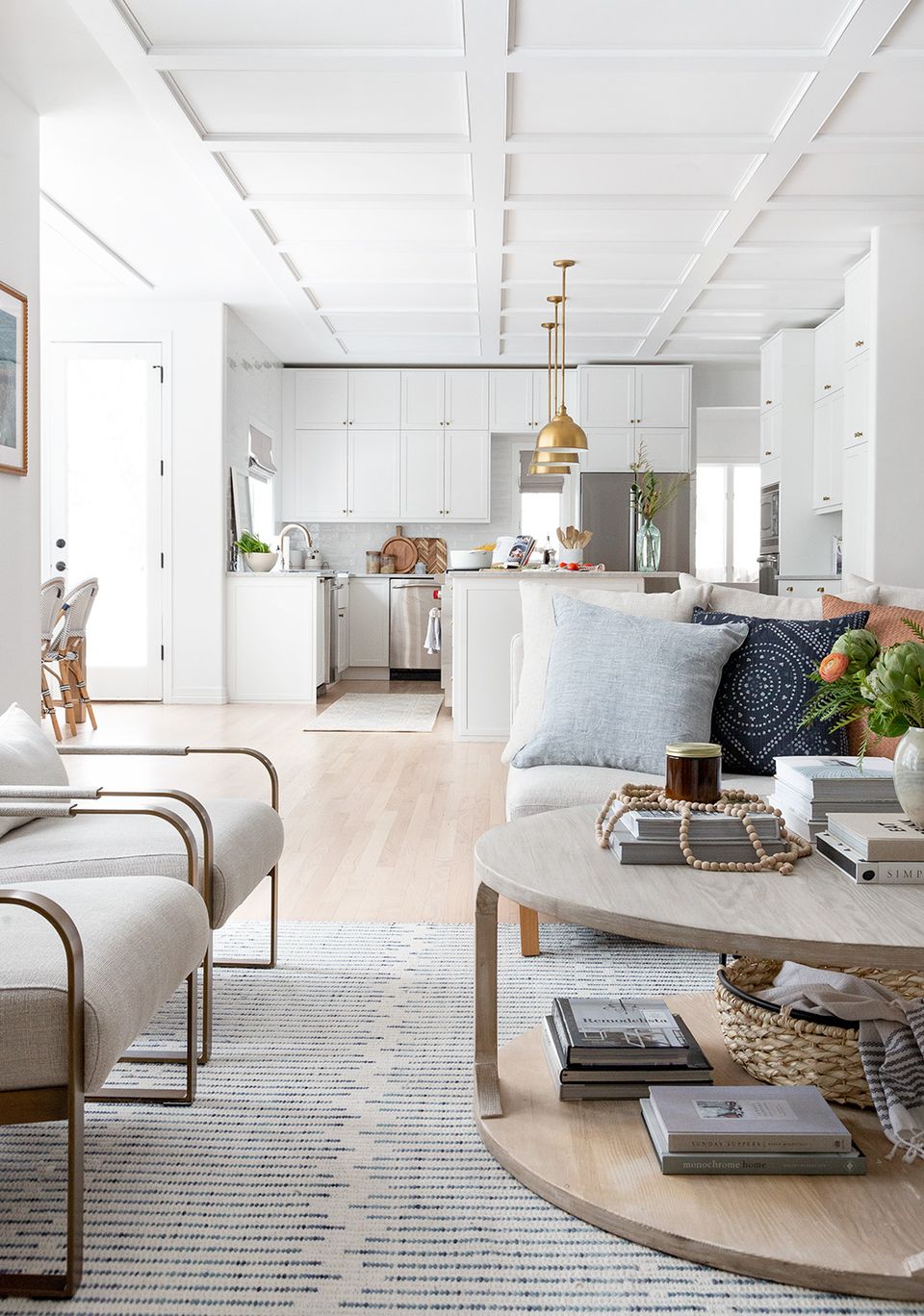Bright farmhouse living space with white coffered ceiling, natural wood accents, and minimalist decor emphasizing clean lines and airy elegance.