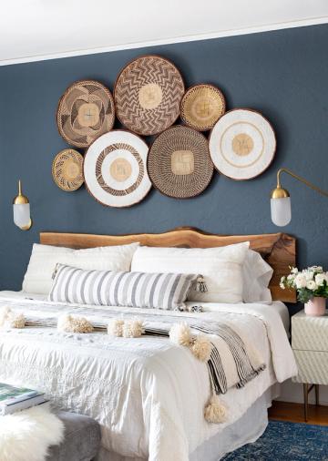 Coastal-inspired bedroom with slate blue accent wall, woven basket wall display, and white bedding with brass accents