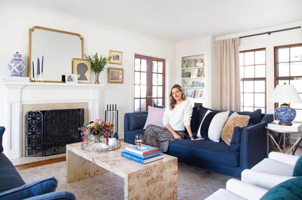Bright transitional living room with navy velvet sofa, white fireplace, warm wood accents, and classic blue-and-white decor.