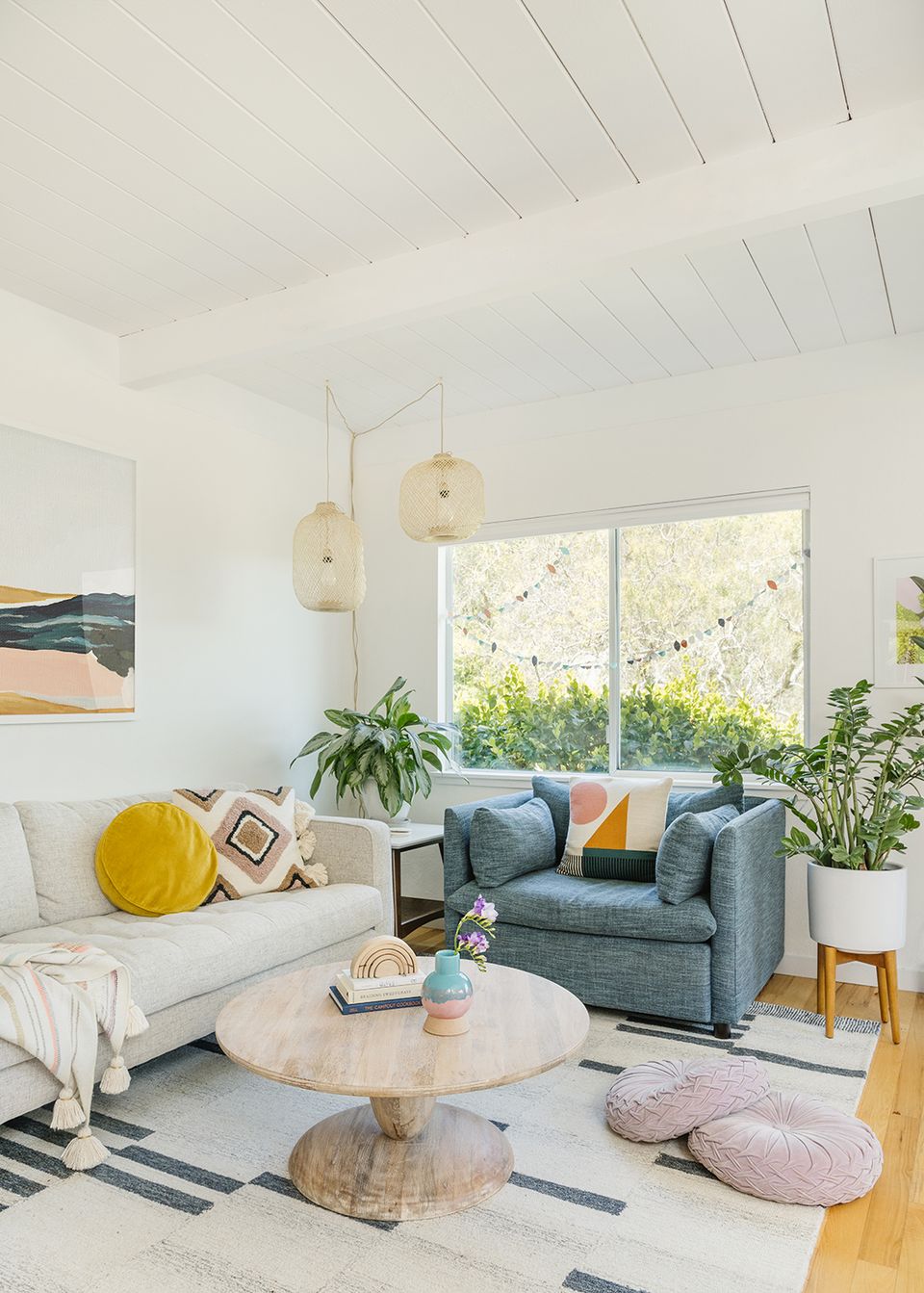 Airy boho space with white vaulted ceiling, slate blue armchair, natural wood tables, and colorful accent pillows