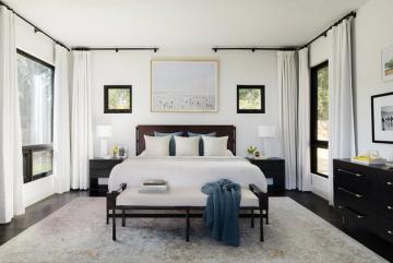 Contemporary black and white bedroom with canopy frame, layered neutral bedding, and symmetrical styling creating calm elegance
