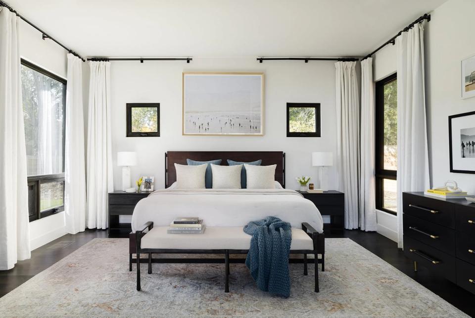 Contemporary canopy bedroom featuring black metal frame, white linens, and symmetrical black nightstands with curated gallery wall and natural light.