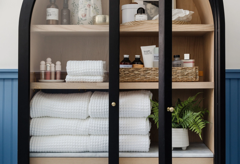 Modern spa bathroom with white stacked towels in black-framed cabinet, blue wainscoting, and botanical accents