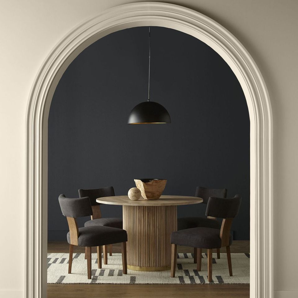 Mid-century modern dining nook with dark gray accent wall framed by archway, natural wood table and black chairs