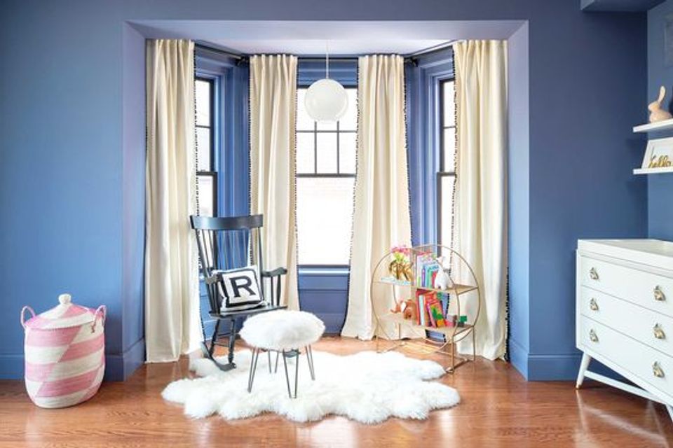 Modern blue bedroom with cream curtains, mid-century seating, and bright window nook