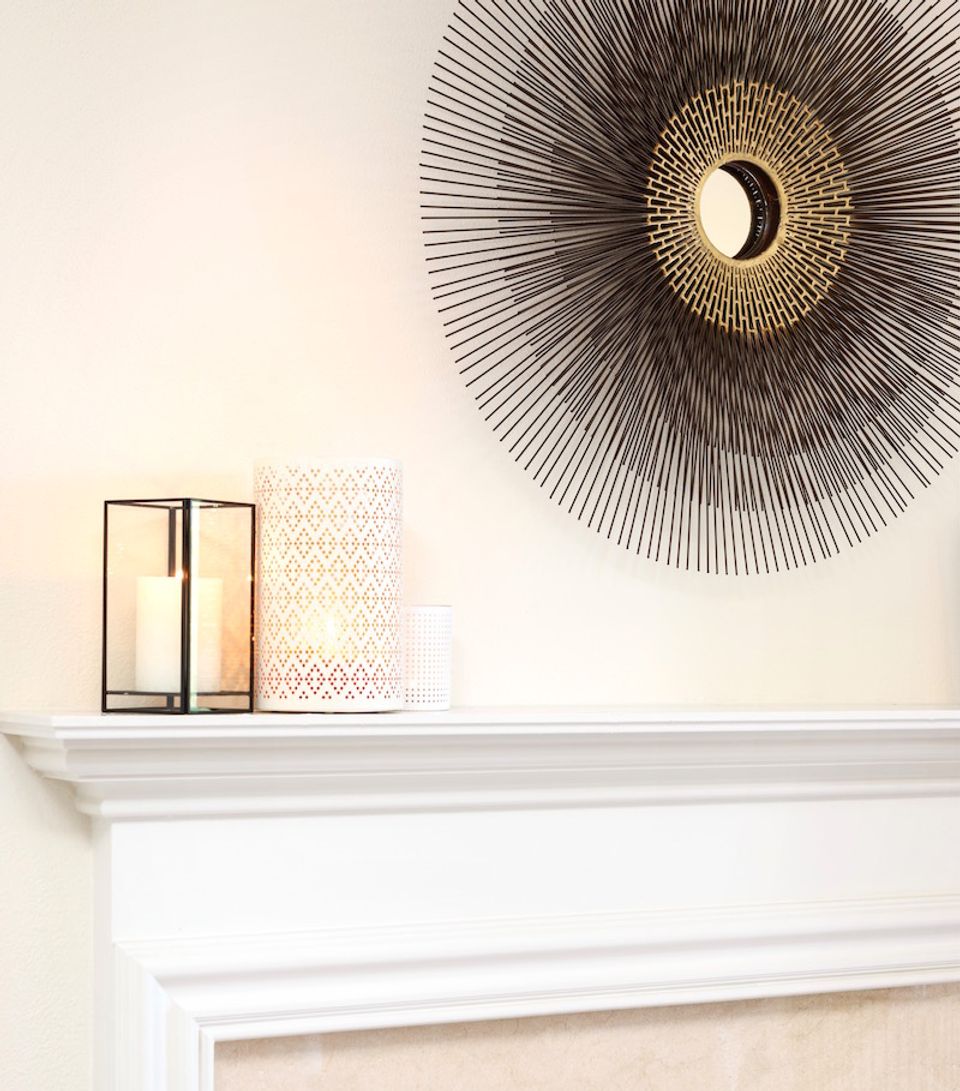 Elegant fireplace mantel with brass sunburst mirror, geometric wall art, and minimalist modern decor in warm cream palette.