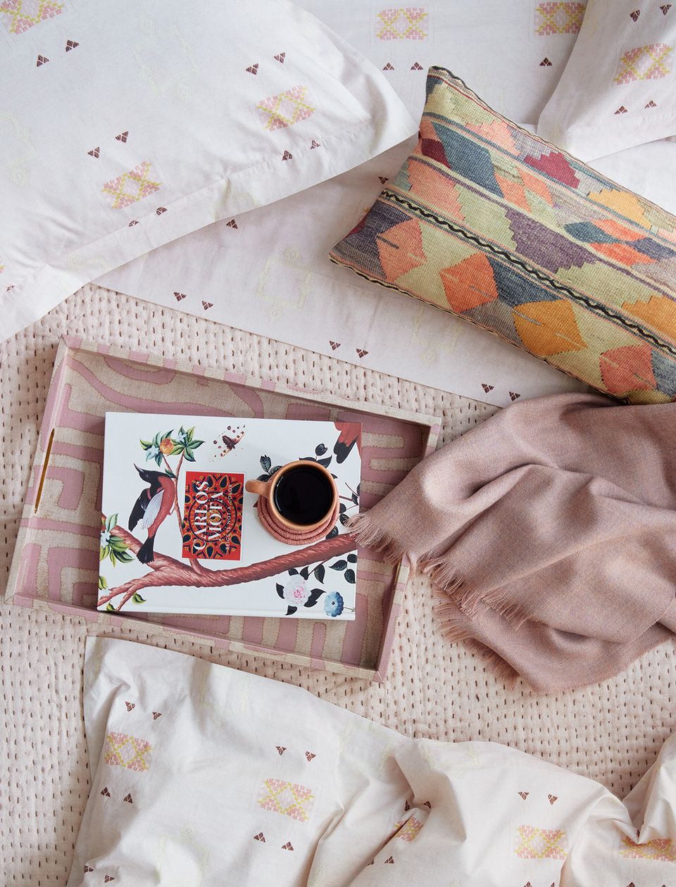 Cheerful pastel bedding flat lay with colorful patterns, pillows, and morning coffee styling