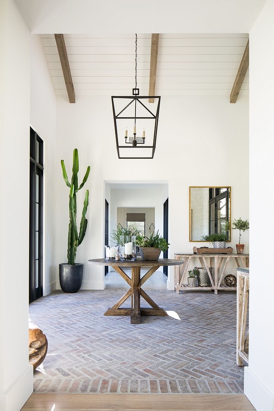 Bright farmhouse entryway with herringbone tile flooring, exposed beam ceiling, black lantern pendant, and modern rustic wood table with greenery.