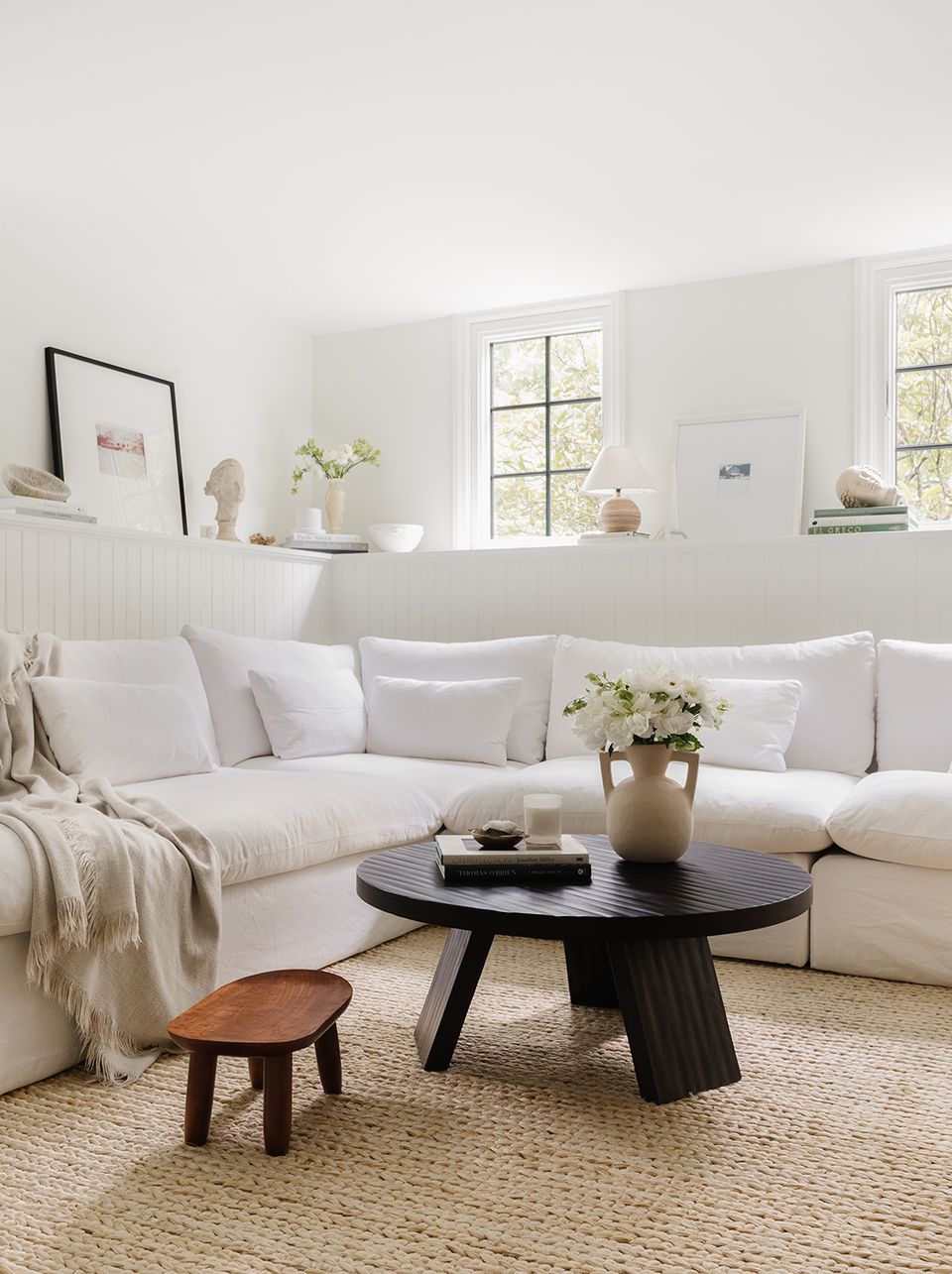 Contemporary living room featuring cream sectional, black round coffee table, and light-filled minimalist atmosphere