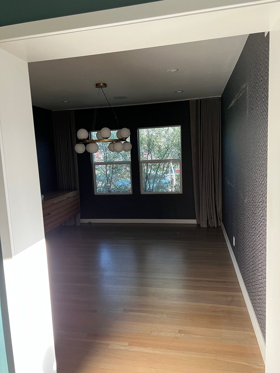 Modern dark moody room with charcoal walls, warm wood flooring, and natural light from large windows