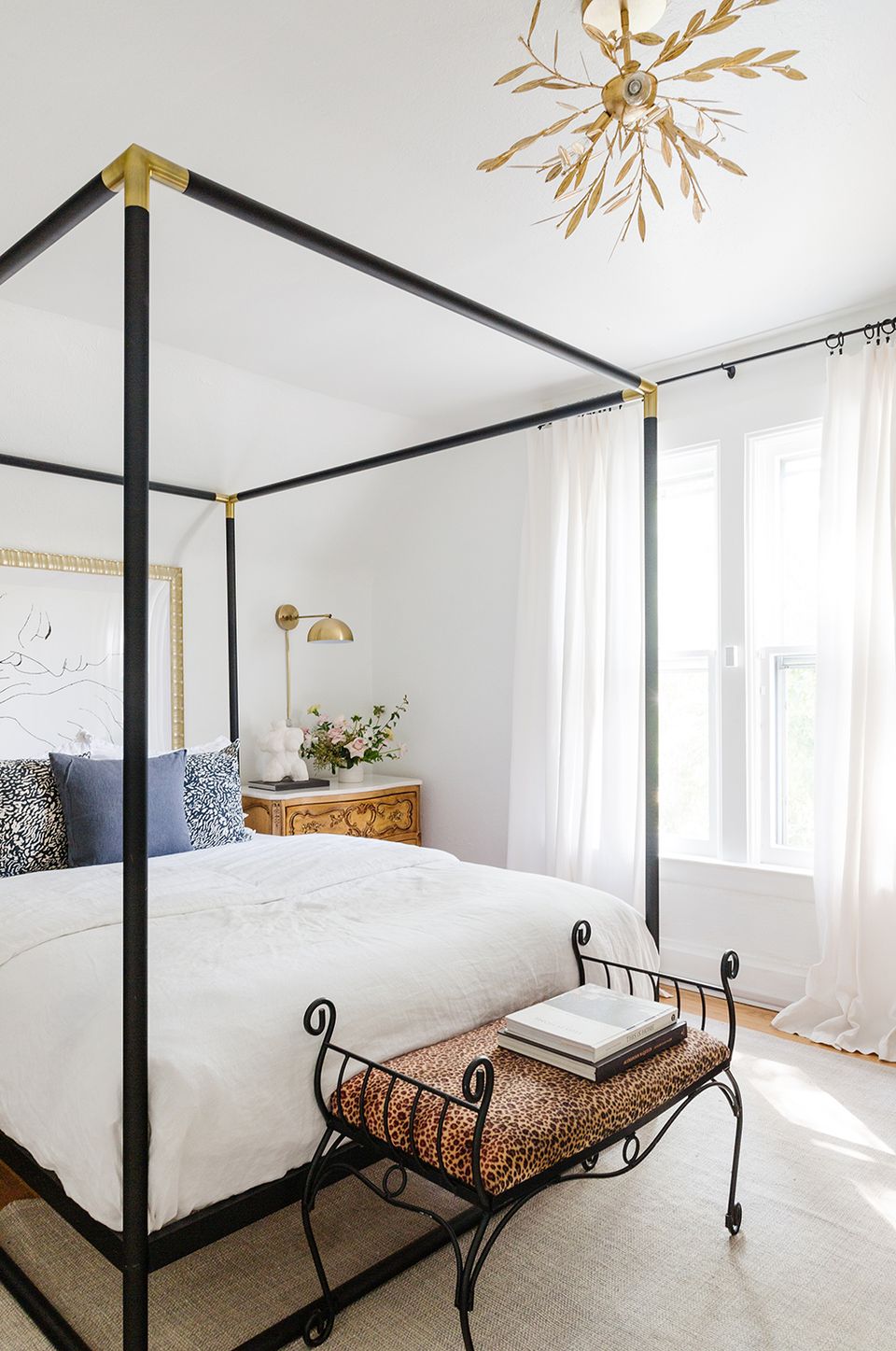 Minimalist bedroom with black canopy bed, brass accents, and natural light from sheer curtains