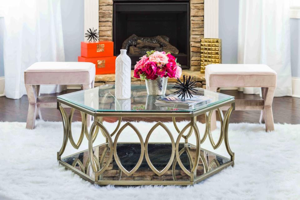 Glam geometric coffee table with glass top and brass-tone metal base in bright, airy living room