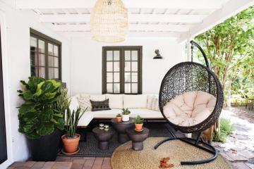 Modern bohemian patio with hanging egg chair, potted plants, and neutral tones creating a relaxed outdoor retreat.