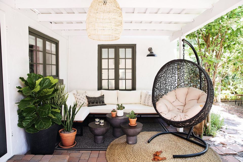 Modern bohemian patio with white walls, black-framed doors, hanging egg chair, lush greenery, and warm neutral furnishings