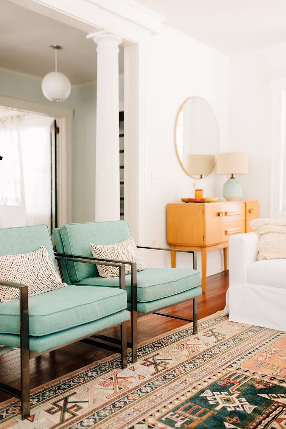 Mid-century modern bedroom with pale cream walls, mint-green chairs, warm wood dresser, and vintage geometric rug for retro charm