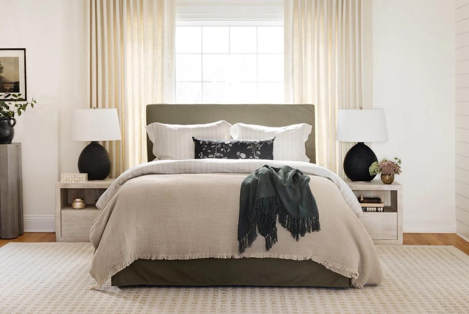 Modern coastal bedroom with neutral beige and charcoal palette, layered pillows, and floor-to-ceiling cream curtains creating serene elegance