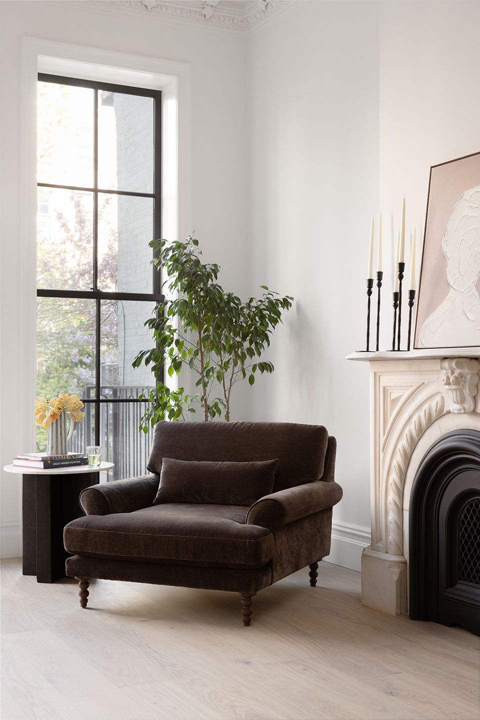 Contemporary fireplace setting with dark charcoal chair, tall plant, and bright grid windows