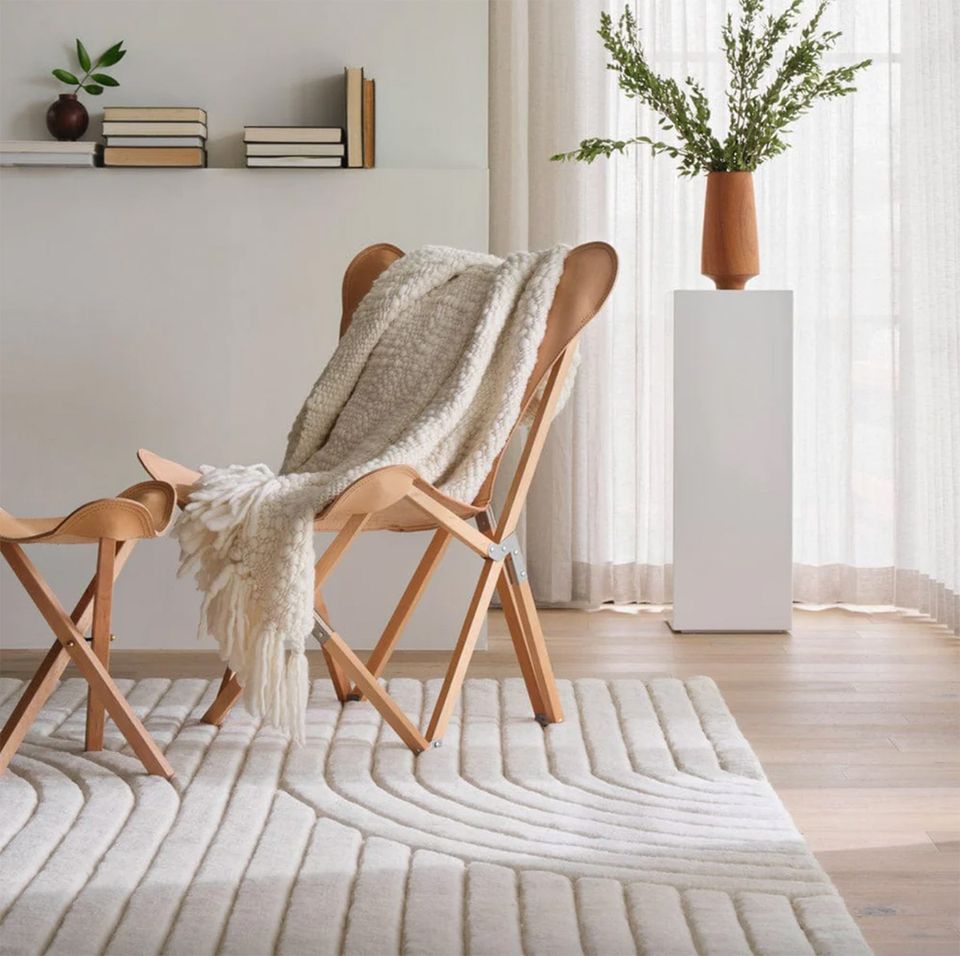Scandinavian reading nook with natural wood frame chair and striped area rug