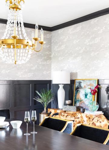 Sophisticated dining space with black shiplap wainscoting, patterned upper walls, and glamorous gold chandelier
