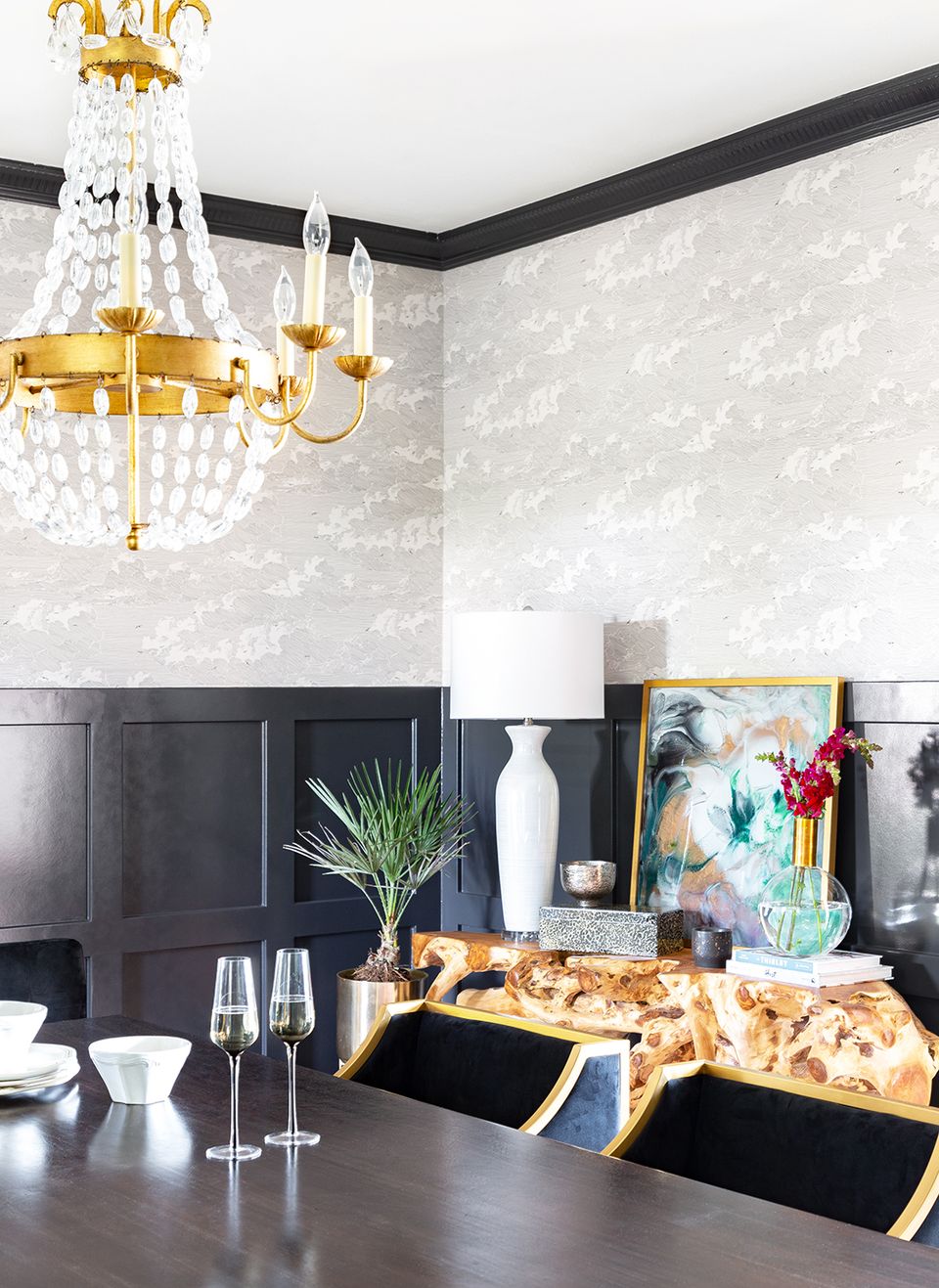Sophisticated dining space with black shiplap wainscoting, patterned upper walls, and glamorous gold chandelier