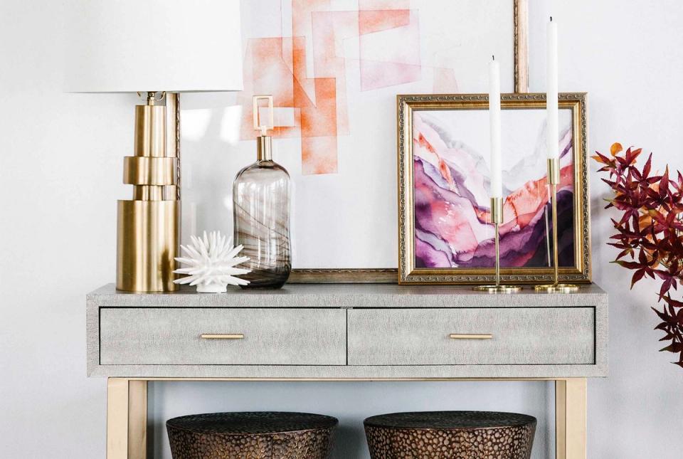 Contemporary console styling with brass elements, watercolor art, and woven baskets