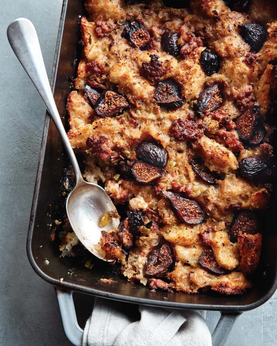 Rustic comfort food styling: golden-brown bread pudding with caramelized figs in dark baking dish, warm autumn palette