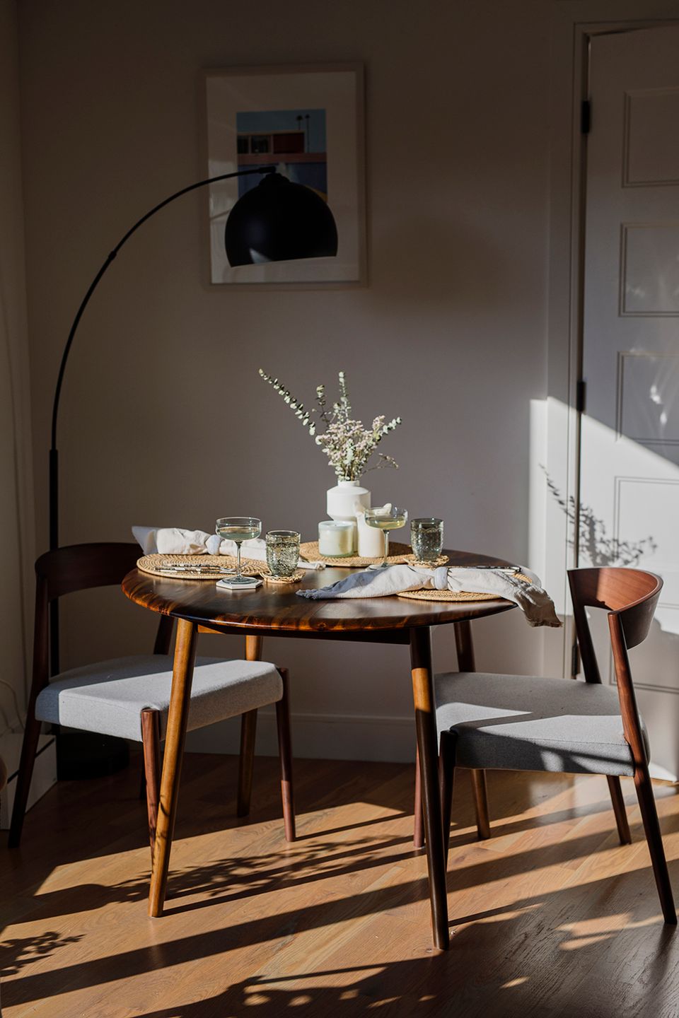Minimalist Scandinavian dining nook with round walnut table, taupe walls, natural light, and understated mid-century modern aesthetic.