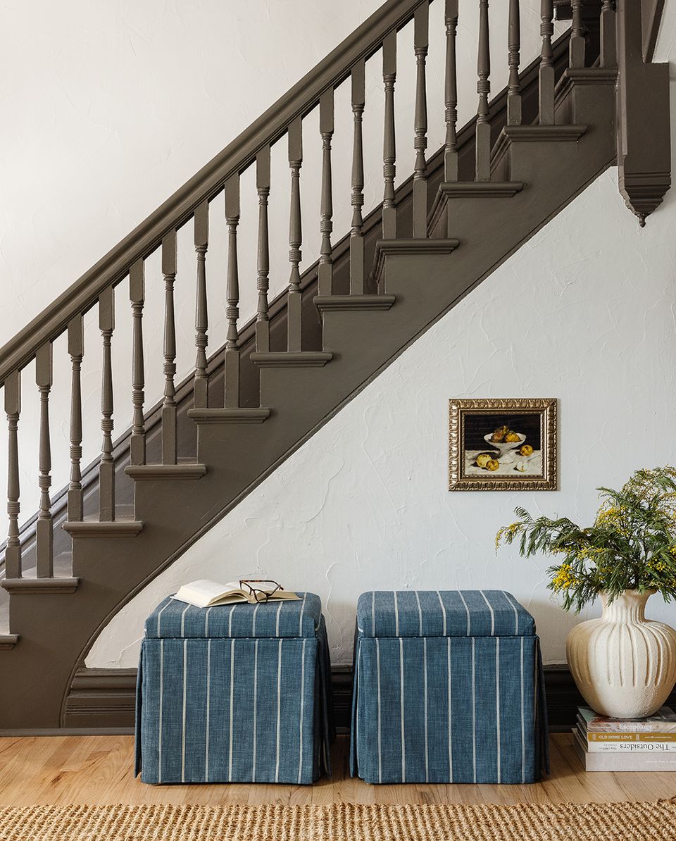 Classic entryway with staircase, blue-striped poufs, natural jute rug, and cream-and-brown traditional palette