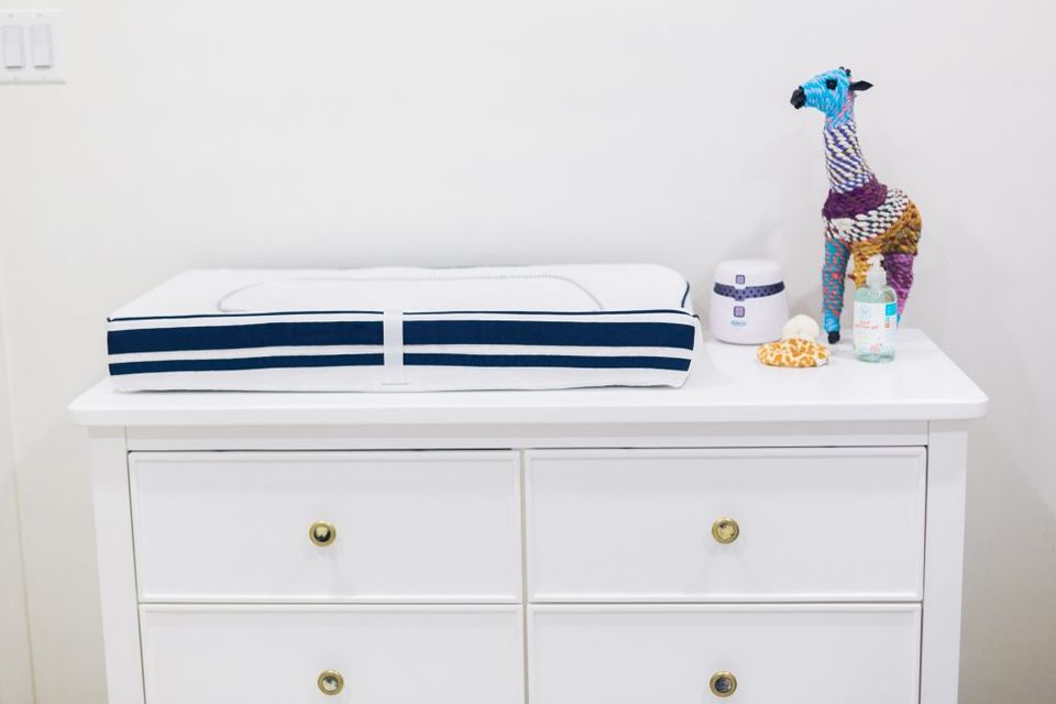 Clean minimalist changing table in white with navy striped changing pad and brass hardware