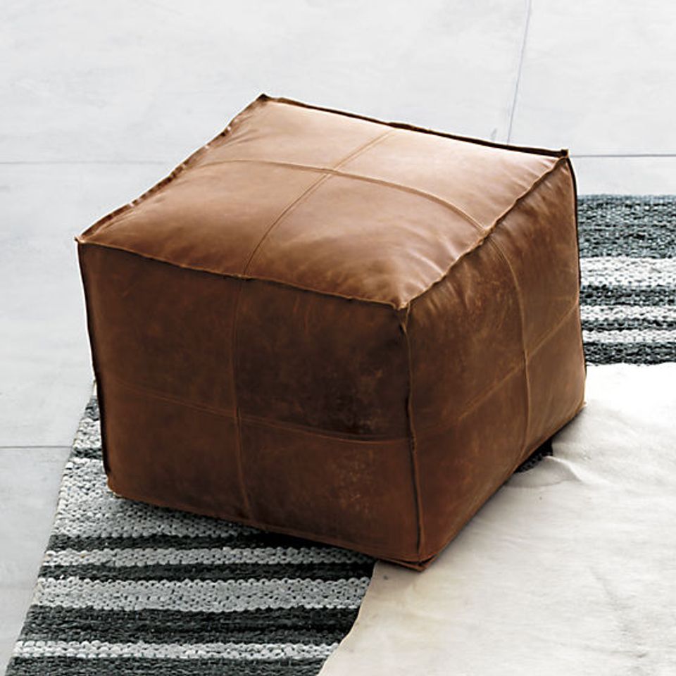 Rich cognac leather cube ottoman on geometric striped rug with soft white tones in modern minimalist setting.