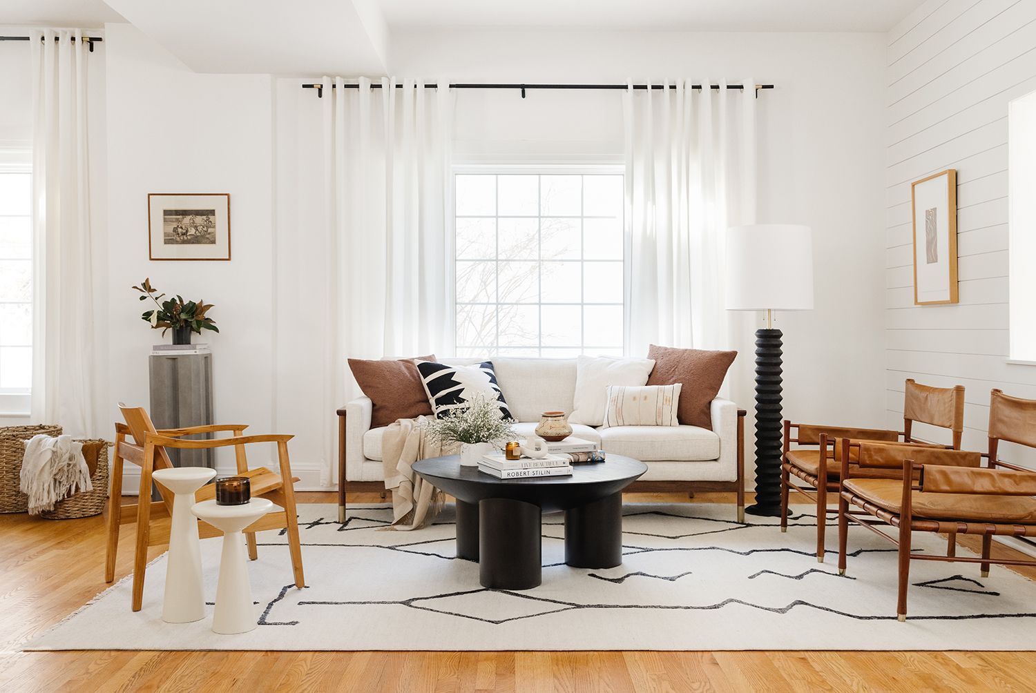Scandinavian living room with cream sofa, wooden chairs, geometric rug, and neutral palette creating airy, cohesive space