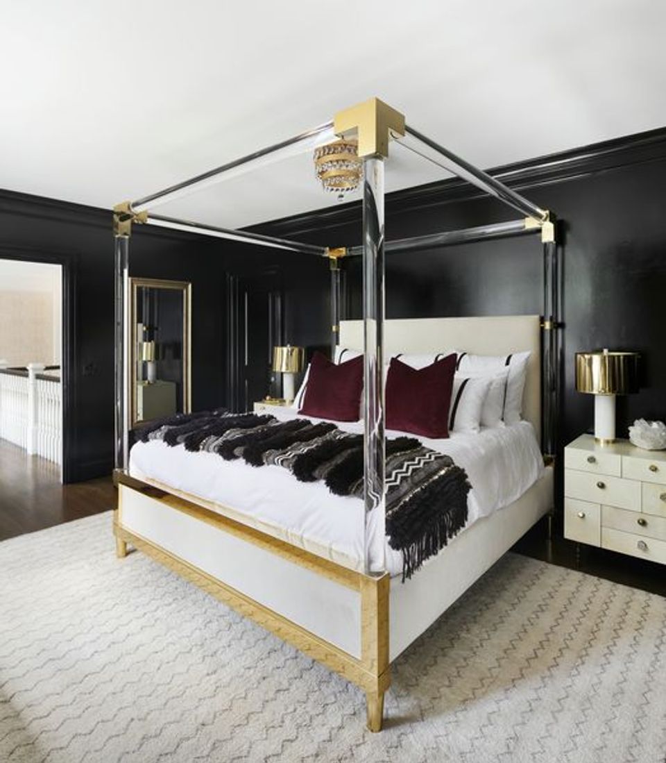 Glam primary bedroom with black walls, chrome canopy bed, burgundy pillows, brass details, white accents