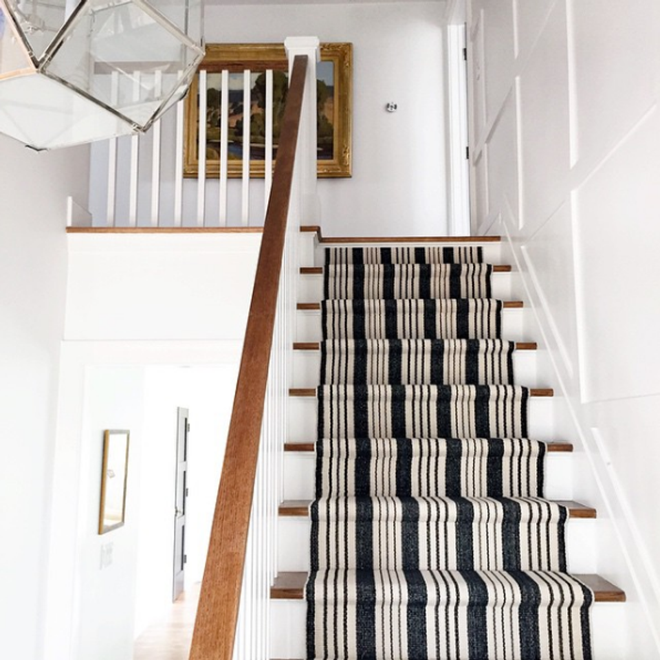 Scandinavian staircase featuring black and cream geometric striped runner, warm wood rails, and minimalist white walls