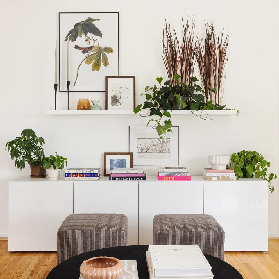 Modern minimalist shelving display with botanical artwork, potted plants, and curated decor on white storage units with natural wood floors