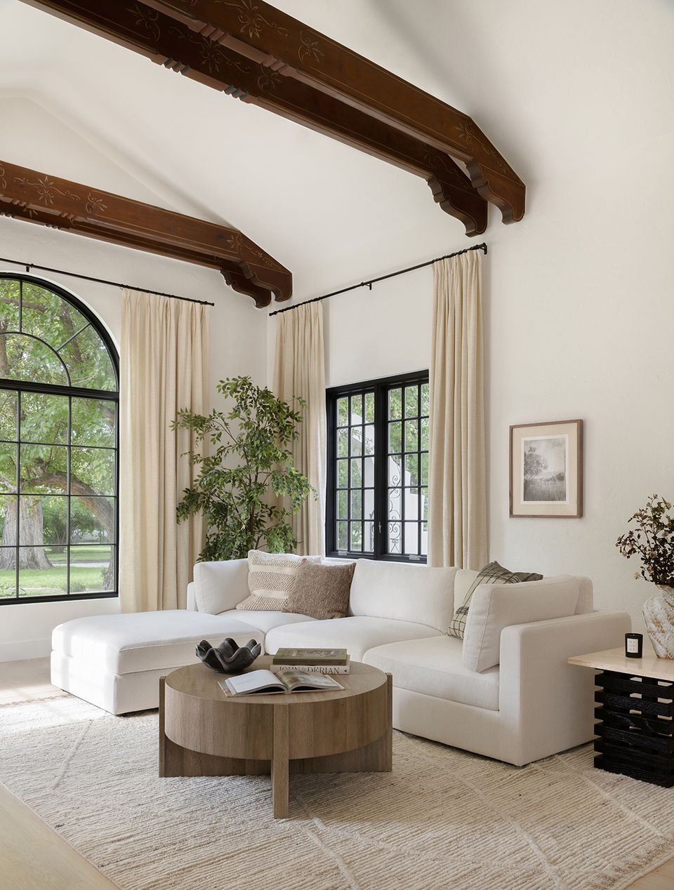 Rustic-modern farmhouse living room featuring exposed dark wood beams, crisp white walls, natural wood accents, and botanical elements.