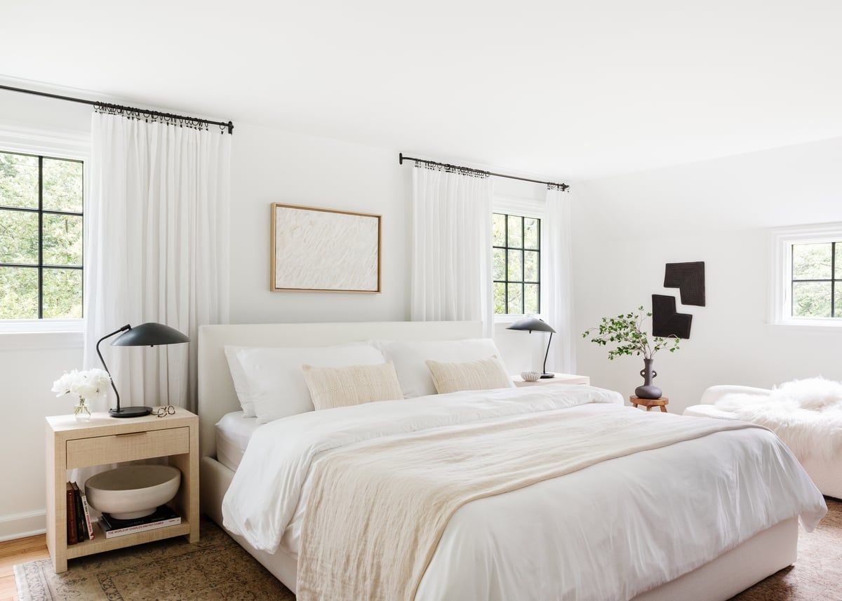 Serene minimalist bedroom with cream and beige bedding, natural wood nightstand, and floor-to-ceiling sheer white curtains creating a calm, Scandinavian aesthetic.