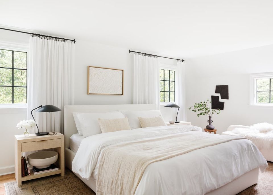 Serene minimalist bedroom with cream and beige bedding, natural wood nightstand, and floor-to-ceiling sheer white curtains creating a calm, Scandinavian aesthetic.