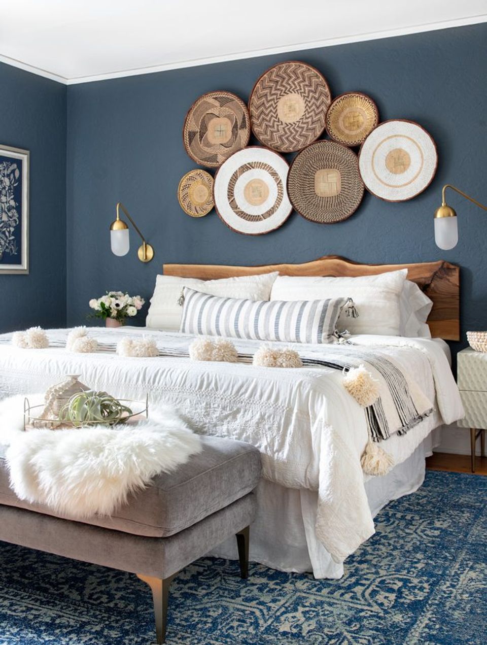 Coastal bedroom with slate blue walls, woven basket wall art, warm wood bed frame, and crisp white bedding.